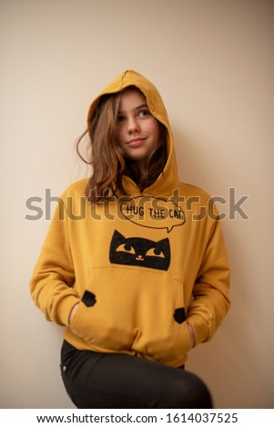 Brunette pretty charming Girl 10 years old wearing loose sweater with dark hair with dark appealing eyes. Pretty girl posing against gray studio wall. Teenager girl in a yellow jacket with dark hair