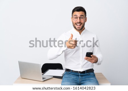 Young businessman holding a mobile phone giving a thumbs up gesture