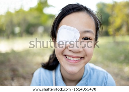 Happy asian child girl cover with blindfolded bandaged eye after surgery or treatment of strabismus,lazy eye, hygienic,prevent infection,protect dust,smiling female people feeling pain,eye injury  Royalty-Free Stock Photo #1614055498