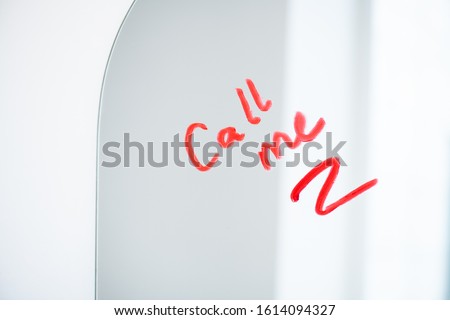 Part of mirror with asking for call written with red or crimson lipstick by amorous young woman