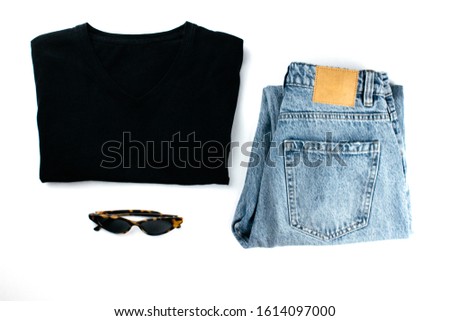 Black cotton t-shirt, blue jeans, sunglasses flat lay on white background. Clothes in minimal style. Stylish modern outfit top view. Template, mockup for advertising, web, social media. Stock photo.