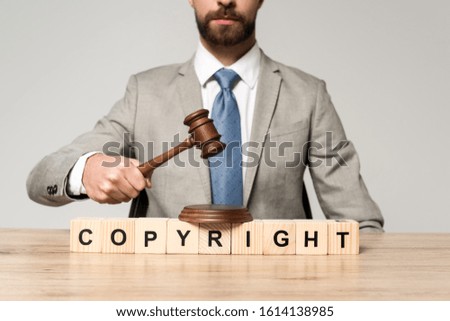 cropped view of judge holding gavel near wooden cubes with copyright inscription isolated on grey