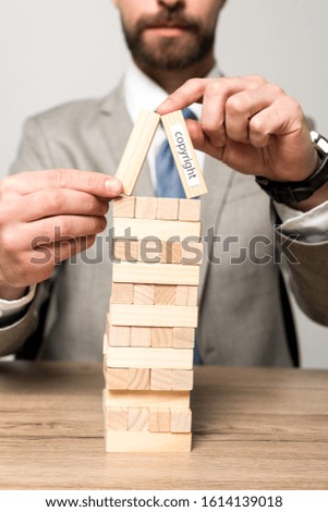 partial view of businessman playing blocks wood tower game with copyright inscription isolated on grey
