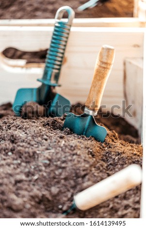 For a gardener. Close up of wooden box with soil and garden spade, shovel prepared for planting vegetables or flowers. Vertical shot. Selective focus