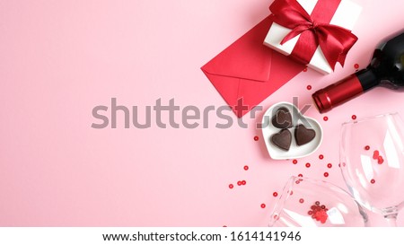 Valentine's day background with wine bottle, gift box, glasses, heart shaped candies, red paper envelope and confetti on pink background. Greeting card template for Valentines Day. Flat lay, top view