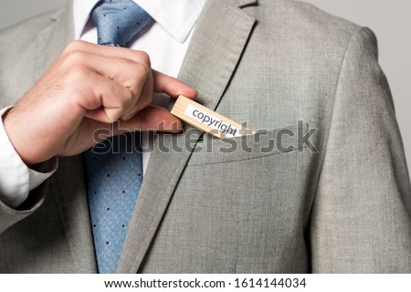 cropped view of businessman putting wooden block with word copyright in pocket isolated on grey