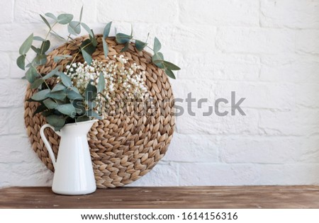 white jug vase with a bouquet of eucalyptus on a wooden table against the background of a white wall.