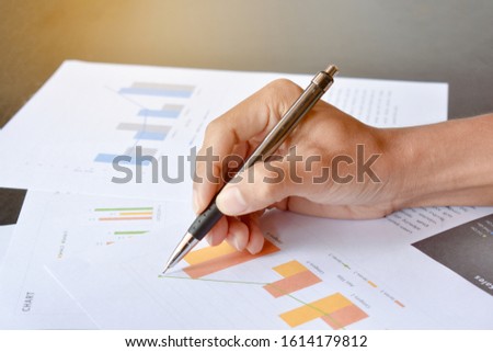 The hand is holding the pen writing business graphs on paper 