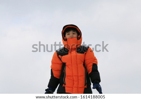The boy in an orange hat and jacket is playing on a small snow covered hill.