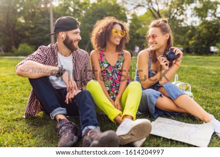 happy young company of talking smiling friends sitting park, man and women having fun together, colorful summer hipster fashion style, traveling with camera