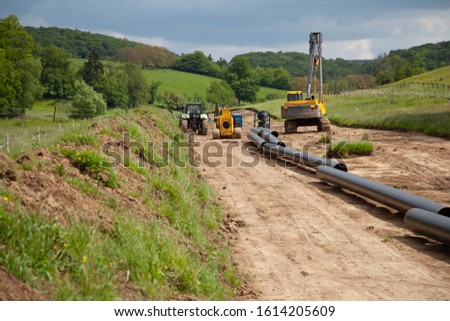 Unplugged gas pipeline in the coutryside diagonally from the right diagonally by photo with gas laying machines in the background