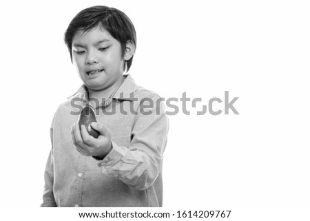 Studio shot of cute Japanese boy holding avocado and looking disgusted