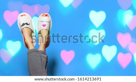 Cute funny couple on blue background with color bokeh hearts. Woman lying with legs upwards wearing unusual slippers with faces of man and woman