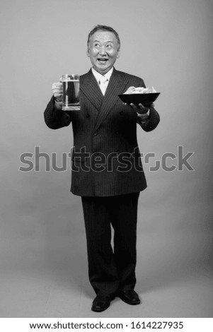Mature Asian businessman holding glass of beer and bowl of potato chips