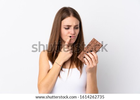 Young woman over isolated white background taking a chocolate tablet and having doubts