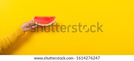 hand holds watermelon slice over yellow background. Summertime concept. Panoramic image with space for text.