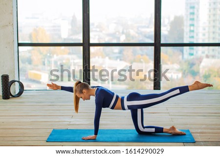 Yoga asana Indoor before a large panoramic window. Sports recreation. Beautiful young woman in yoga pose. Individual sports. Royalty-Free Stock Photo #1614290029