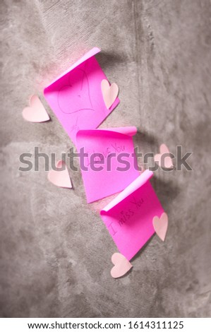Sticky notes in pink with a Declaration of love, decor in the form of small hearts of paper on the concrete gray. Create a romantic mood for Valentine's day. reminder notes