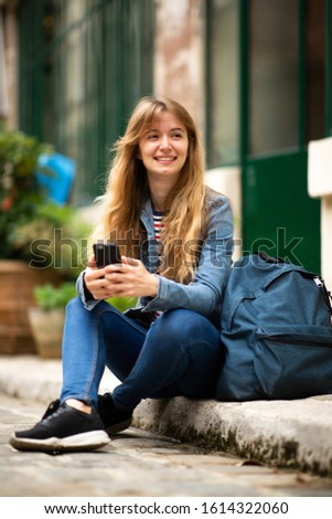 Portrait female college student sitting outside with cellphone and bag
