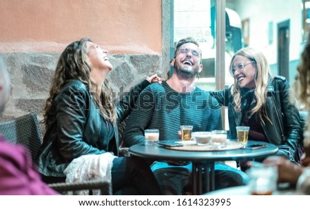 Young friends having genuine fun drinking on happy hour at street bar - Millenial people laughing and spending time together - Friendship lifestyle concept on desaturated neon filter 