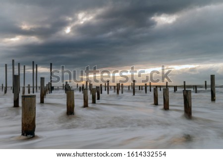 Poles on the beach of Petten Netherlands during sunset and strong wind, a piece of art in the sand