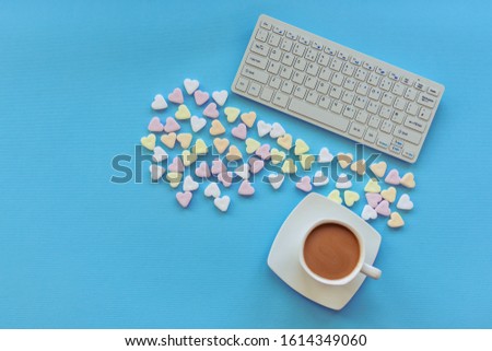 A cup of coffee, candies in a shape of hearts and keyboard on blue table. Top view, flat lay, copy space.
