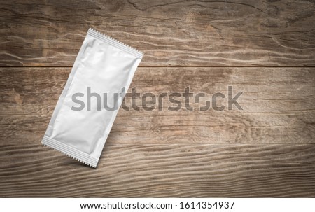 Blank White Condiment Packet Floating on Aged Wood Background.