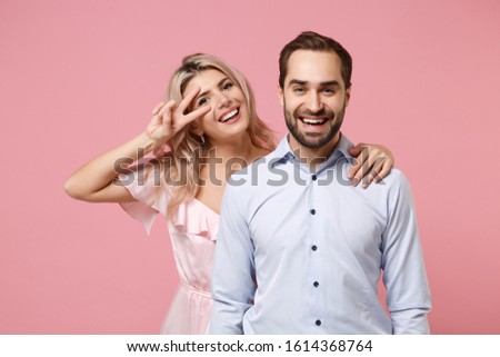 Cheerful young couple two guy girl in party outfit celebrating posing isolated on pastel pink background. People lifestyle Valentine's Day Women's Day birthday holiday concept. Showing victory sign