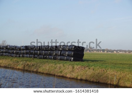 Bales of hay, silage bales, stacked on the grass in a meadow along a ditch wrapped in black plastic. Pasture landscape in the Netherlands near the village of Bergen. Photo January 13, 2020.
