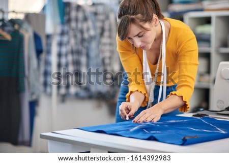 Creative caucasian fashion designer standing in her studio and drawing scheme on blue linen for a beautiful evening dress.