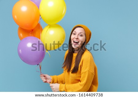 Excited young woman girl in sweater hat posing isolated on blue background studio portrait. Birthday holiday party, people emotions concept. Mock up copy space. Celebrating hold colorful air balloons