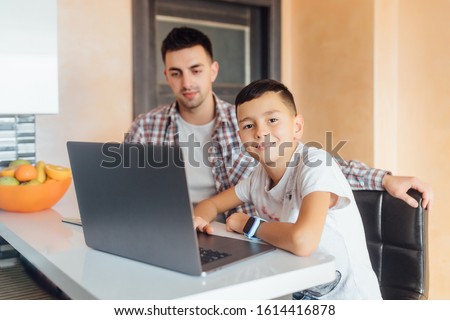 Young kid son with dad using laptop at home for child education, looking at pc screen doing online shopping at home.