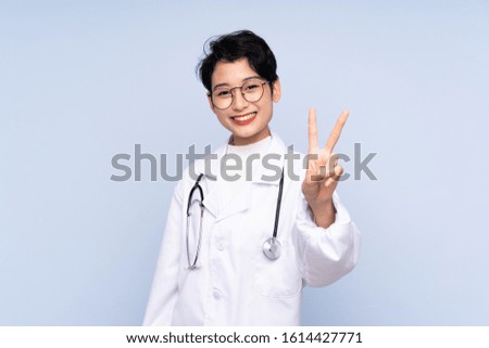 Doctor Asian woman over isolated blue background smiling and showing victory sign