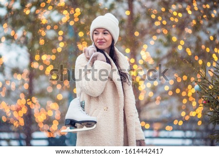 Happy young woman with skates ready to skate on ice rink