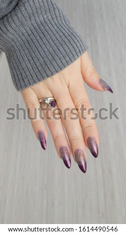 Female hand with long nails and a bottle of blue lilac color nail polish