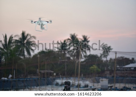 White drone take off from land and flying for take aerial photo. above fish farm coconut background at sunset evening orange sky.
