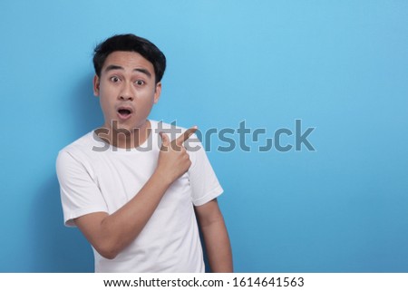 Portrait of happy cheerful Asian young man pointing to the side, surprised and smiling expression, presenting something with copy space, marketing advertising template concept