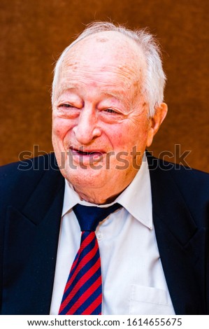 Portrait of happy white elderly man with dark suit, white shirt and striped blue red tie smiling on bright brown background Royalty-Free Stock Photo #1614655675