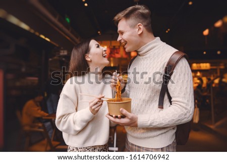 newlywed couple eating noodles with chopsticks in Shanghai outside a food market near Yuyuan. Couple eating authentic local food. husband and wife eating chinese food outisde of a food hall Royalty-Free Stock Photo #1614706942