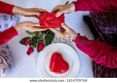 Holding and giving heart shape red cake with hands for Valentine’s day. Celebration on the bed concept with a cake and red roses. 