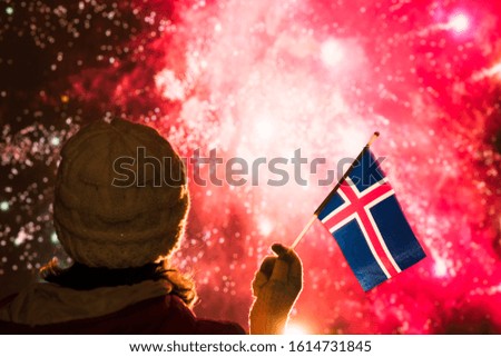 Fireworks at night. Woman in winter clothes with  flag of Iceland on the New Year.  
