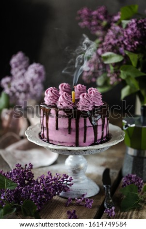 On the table is a beautiful chocolate cake and a bouquet of lilacs.