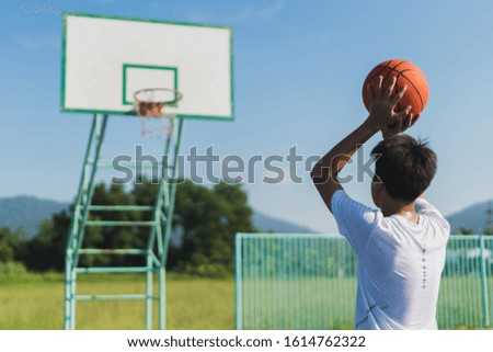 Rear view of a male player throwing the ball into the basketball net on outdoor court