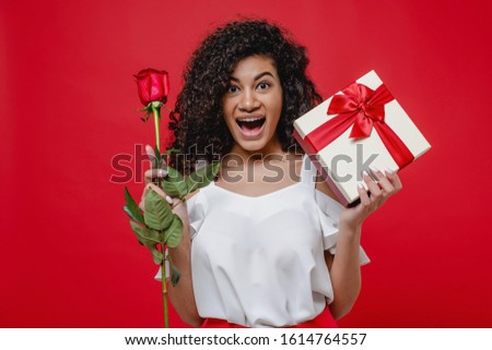 happy smiling black girl with rose and gift box isolated over red
