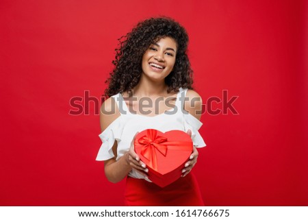 beautiful happy african woman holding heart shaped valentine gift box isolated on red