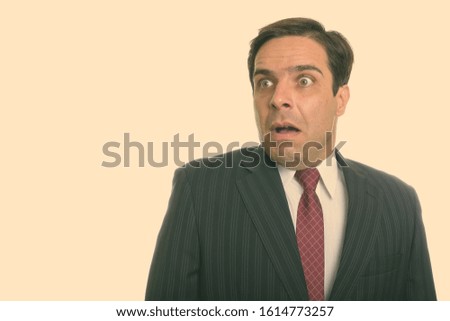 Studio shot of young Persian businessman thinking while looking shocked
