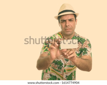 Studio shot of young Persian tourist man taking picture with mobile phone