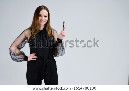 A photo of a pretty smiling brunette girl with excellent makeup in dark clothes is standing on a white background with emotions. Concept portrait for a banner.