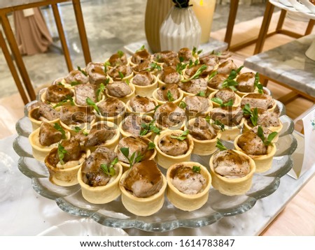 Beautifully decorated catering banquet table with small bites of snacks and appetizers with role of chicken served on glass plate.