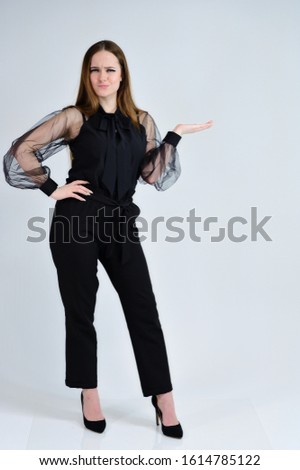 A full-length photo of a pretty smiling girl A brunette girl with excellent makeup in dark clothes is standing on a white background, talking with emotions. Concept portrait for a banner.